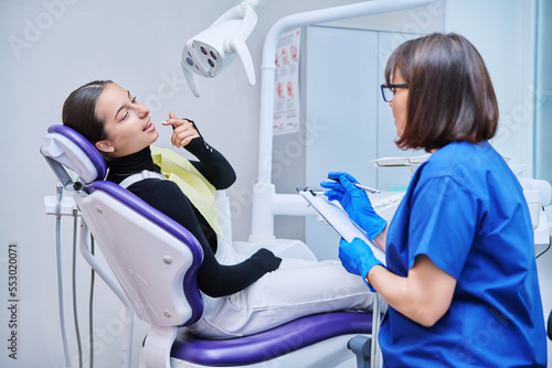Talking dentist and teenage girl patient in dental clinic
