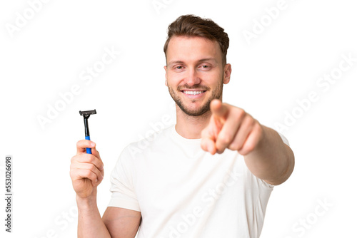 Young caucasian man shaving his beard over isolated chroma key background points finger at you with a confident expression