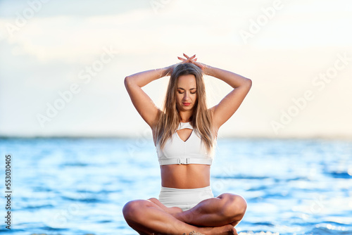 athletic young woman meditating on the shore of a large lake. © yurolaitsalbert