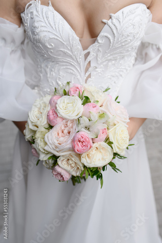 The bride in a beautiful wedding dress holds a wedding bouquet of roses, freesias, peonies in front of her. Wedding day.