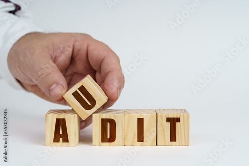 On a white surface, a man stacks cubes with the inscription - AUDIT