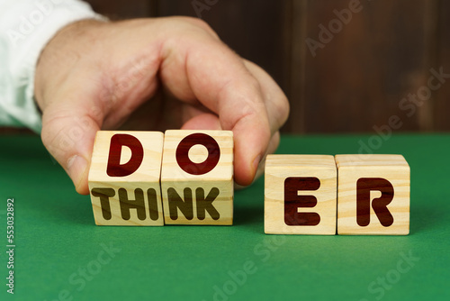 On a green surface, a man puts cubes with the inscription - DOER, THINKER