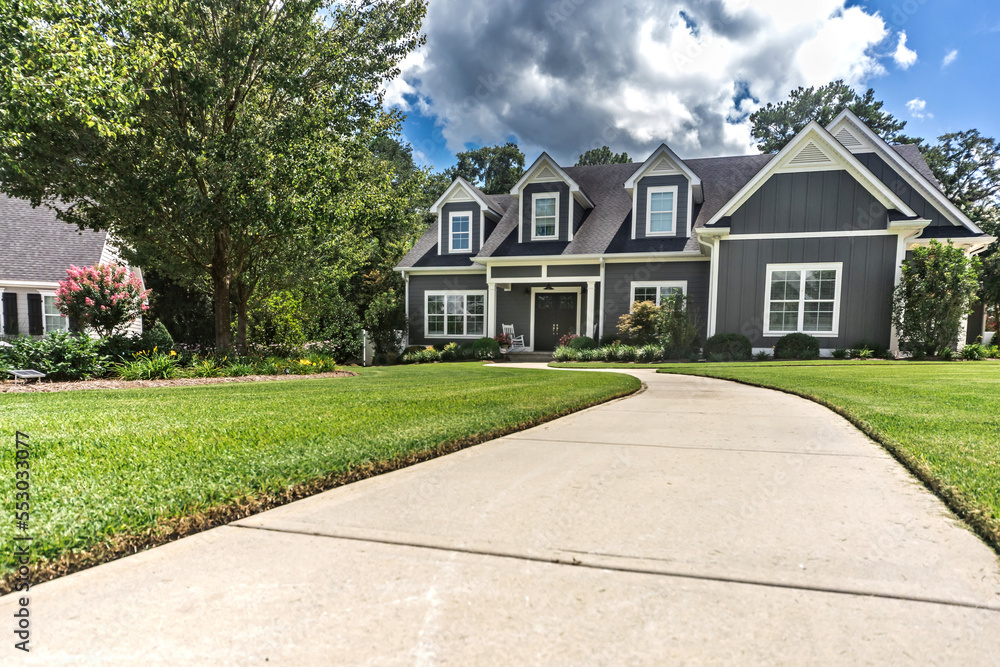 A large gray craftsman new construction house with a landscaped yard and leading pathway sidewalk