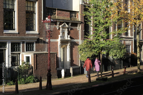 Amsterdam Oudezijds Achterburgwal Canal Street View with House Facades, Autumn Trees and Walking Women, Netherlands photo