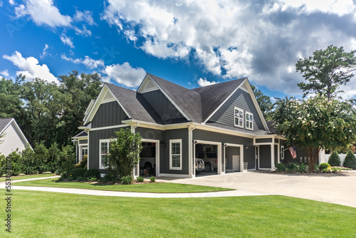 Fototapeta Naklejka Na Ścianę i Meble -  The side view of a large gray craftsman new construction house with a landscaped yard a three car garage and driveway