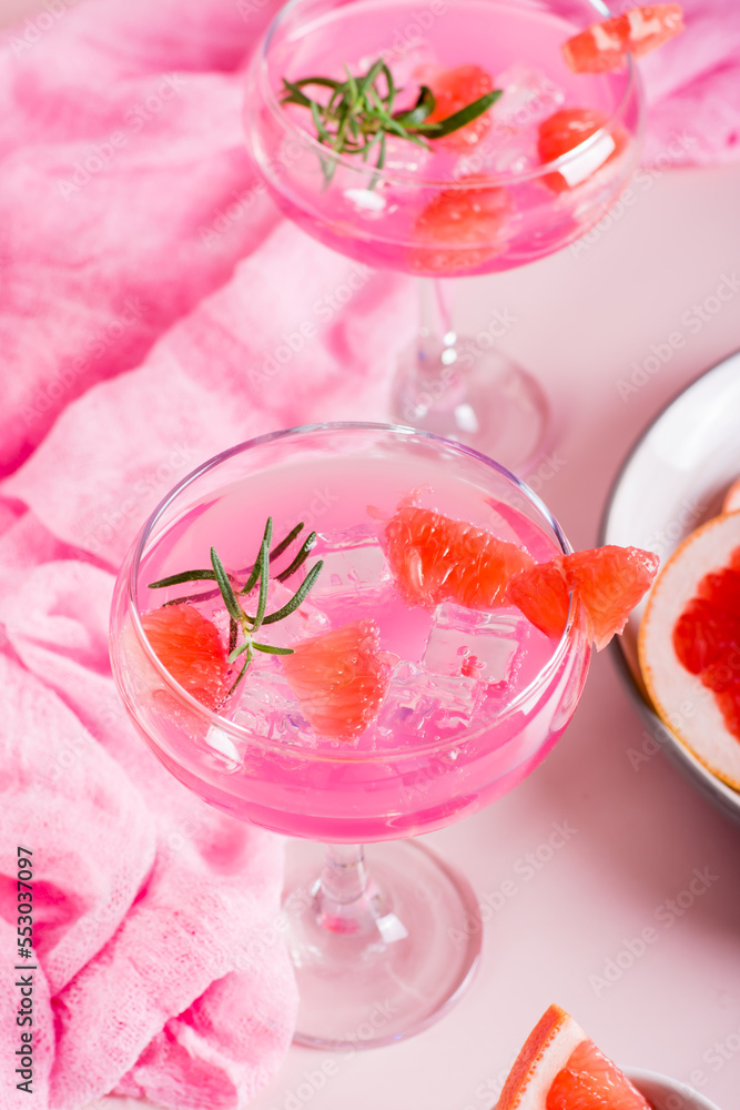 Homemade pink cocktail with ice and rosemary in glasses on the table. Vertical view Homemade pink cocktail with ice and rosemary in glasses on the table. Vertical view