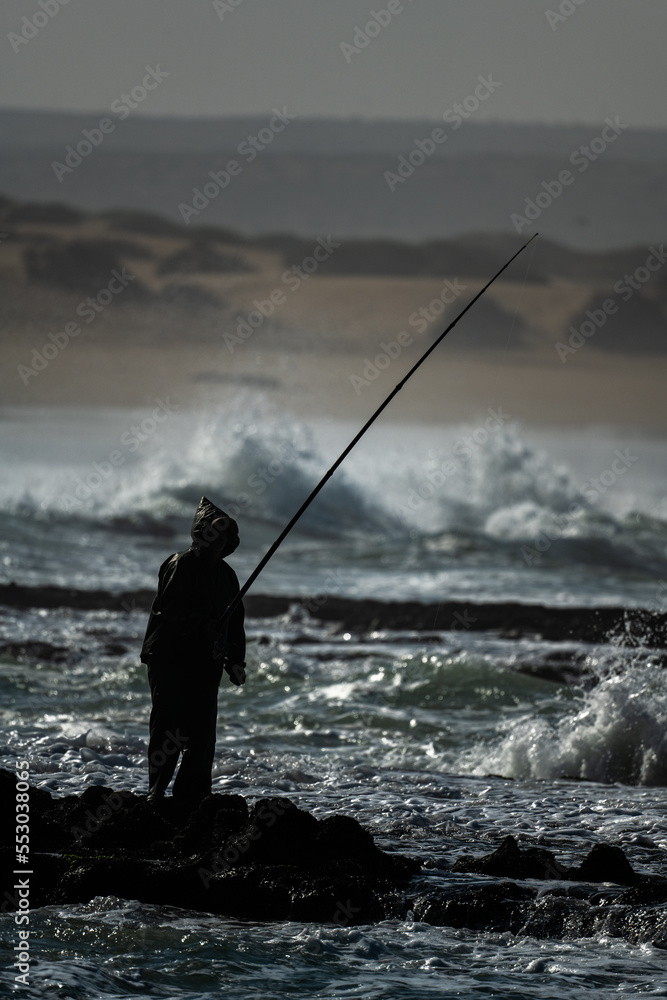 Silhouette of a man fishing in the Atlantic Ocean during high tide.