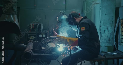 Professional welder is sitting in the workshop at the factory. Work by electric arc welding.