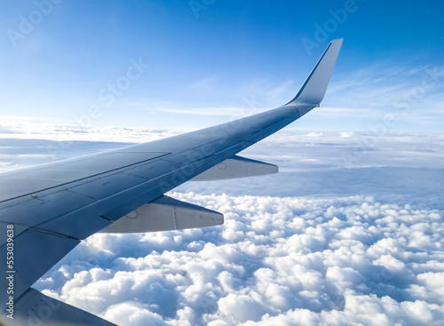 Airplane wing over clouds and sunny blue sky. Aerial view from an aircraft of an overcast sky with stratus cumulus until the horizon