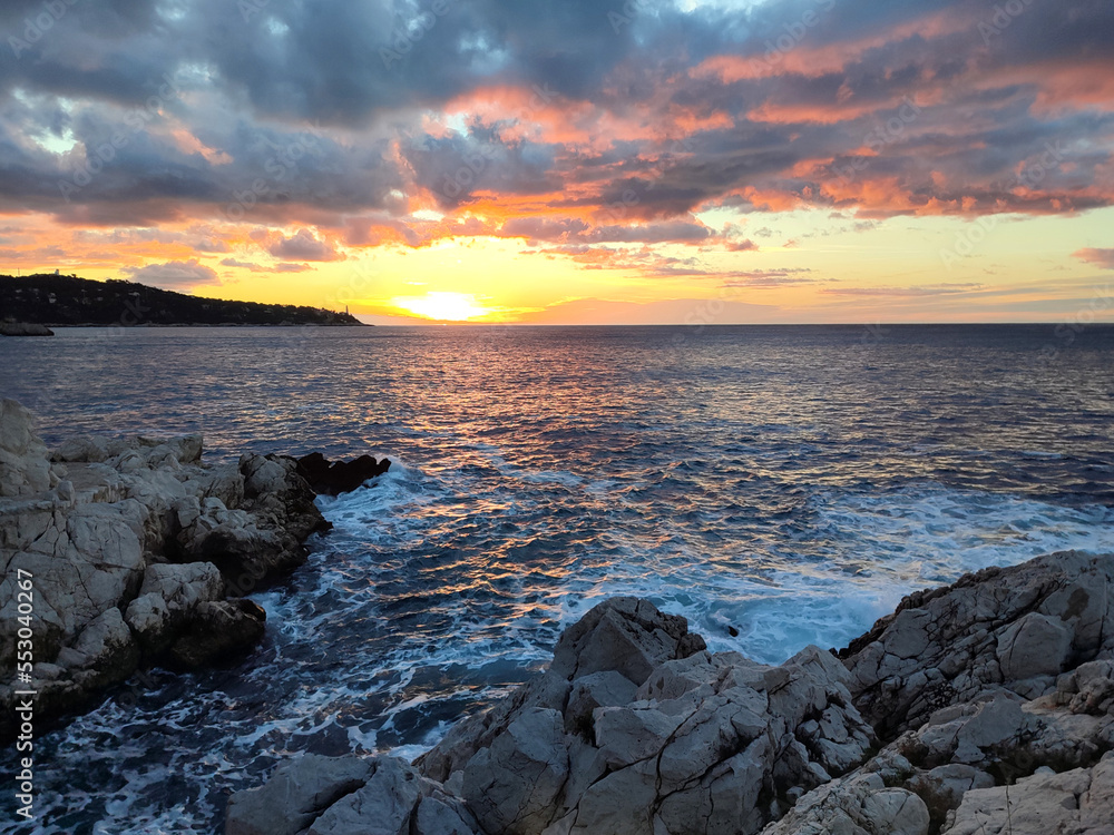 Coucher de soleil sur la mer avec des rochers au premier plan et des nuages colorés