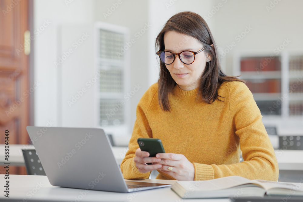 confident woman works in library, in coworking at laptop or office. female student is studying online, female student or business person is talking on phone or chatting. happiness, success