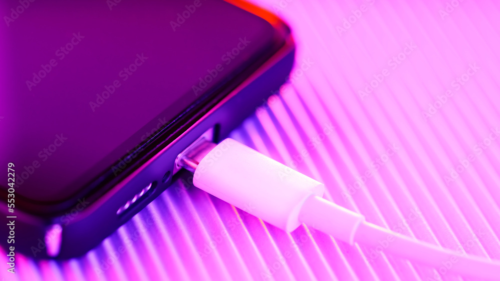 Smartphone charging on a purple background. Mobile phone with connected usb cable for battery charging. Fast charging concept Smartphone charging on a purple background. Mobile phone with connected usb cable for battery charging. Fast charging concept