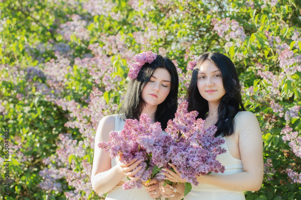 Fototapeta premium two young girls with blooming lilac in sunlight