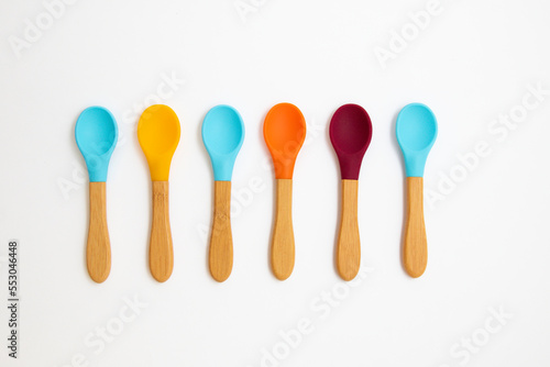 Six silicone spoons with bamboo handles of different colors on a white background. Cutlery is safe for babies