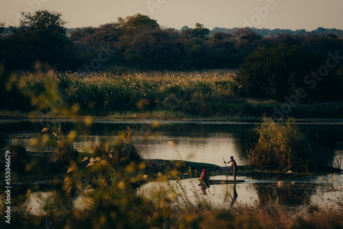 Idyllische Abendszene am Okavango - Zwei Jungen paddeln im Dämmerungslicht mit Einbaum Boot über den Fluss, Rundu, Namibia photo