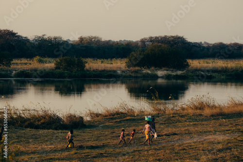 Abendszene am Okavango - Mutter läuft mit ihren Kindern im Dämmerungslicht, nachdem sie sich am Fluss gewaschen haben, nach Hause, Rundu, Namibia