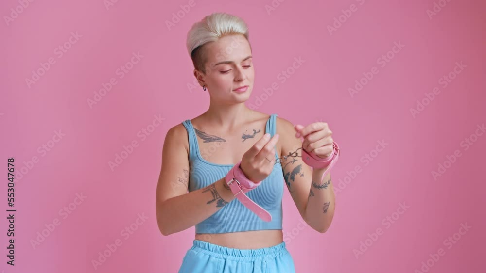 Portrait view of the playful blonde woman looking at her pink handcuffs for bdsm Portrait view of the playful blonde woman looking at her pink handcuffs for bdsm