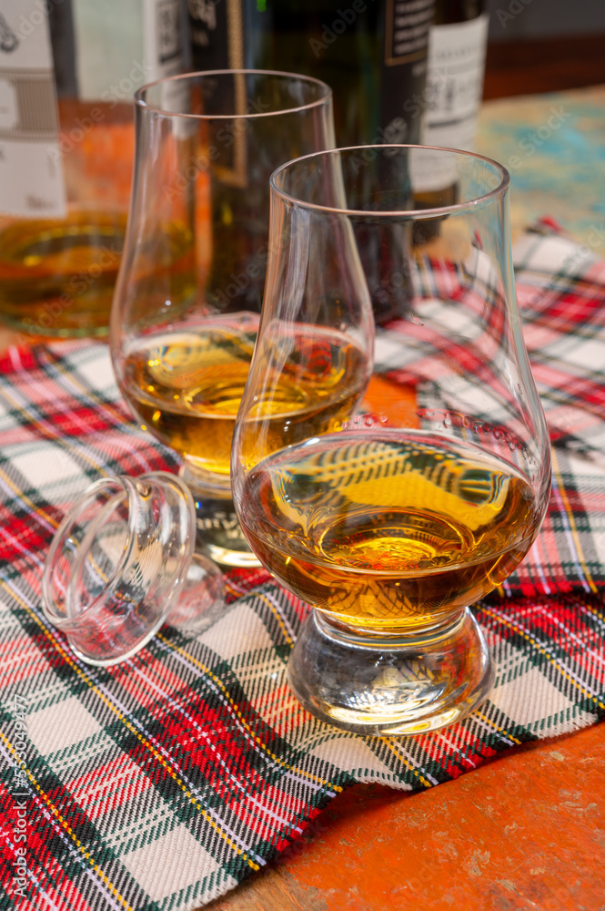 Tulip-shaped tasting glass with dram of Scotch single malt or blended whisky on wooden table with tartan Tulip-shaped tasting glass with dram of Scotch single malt or blended whisky on wooden table with tartan