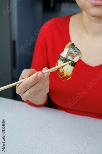 A girl in a red sweater holds sushi with conger eels with chopsticks. Seafood