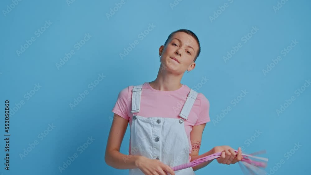 Portrait of thoughtful charming woman holding pink whip while selecting bdsm toys in sex shop Portrait of thoughtful charming woman holding pink whip while selecting bdsm toys in sex shop