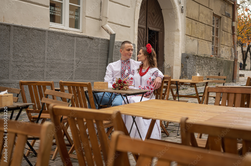 a young couple in national clothes, an embroidered woman sits at a wooden cafe table a young couple in national clothes, an embroidered woman sits at a wooden cafe table