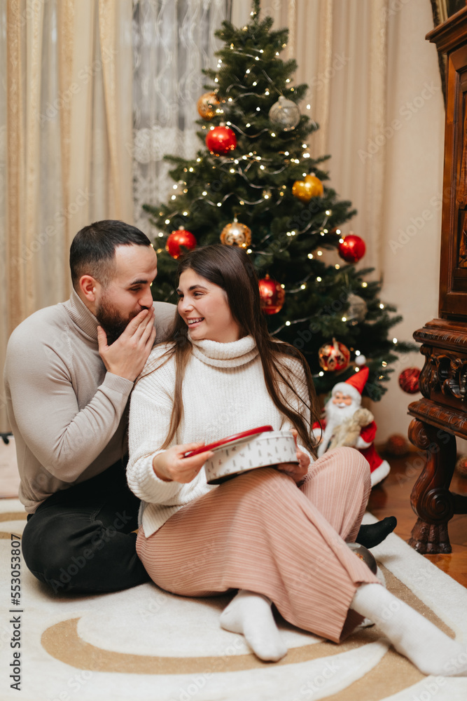 Surprised couple is opening Christmas gift box near the  Christmas tree at home at Christmas. 