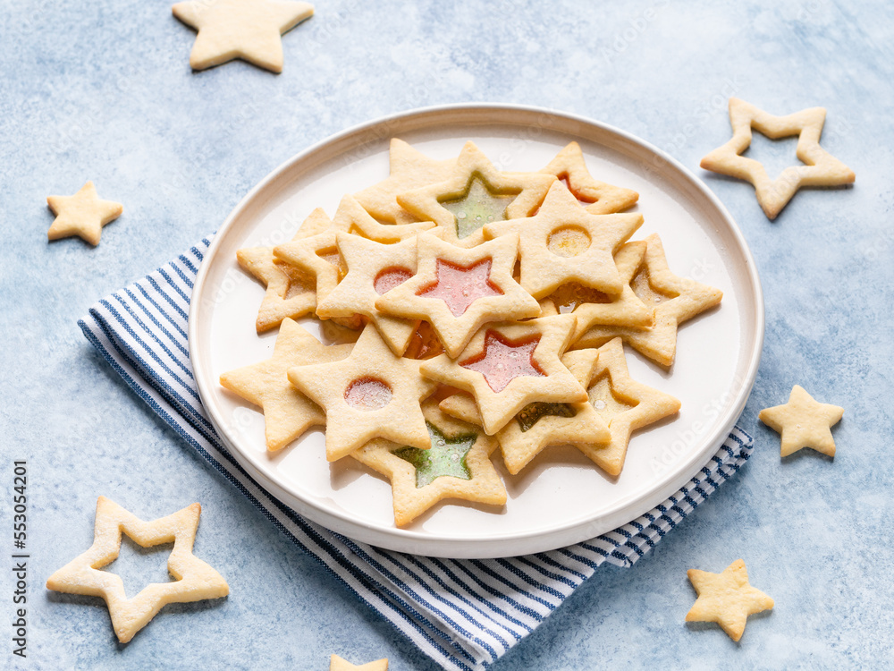 Christmas cookies. Star shaped butter cookies with melted candies (colorful bonbons) inside. Christmas and new year dessert. Close up view. Blue background. Christmas cookies. Star shaped butter cookies with melted candies (colorful bonbons) inside. Christmas and new year dessert. Close up view. Blue background.