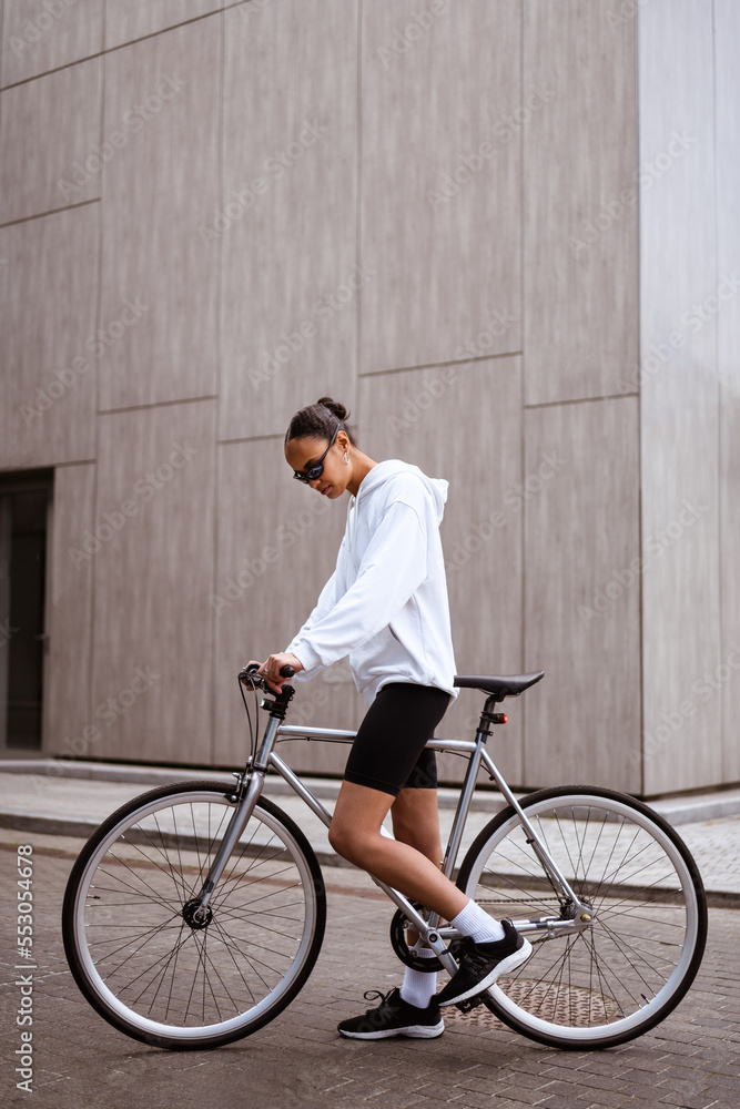 Stylish african american woman in sunglasses standing near bike on city street Stylish african american woman in sunglasses standing near bike on city street