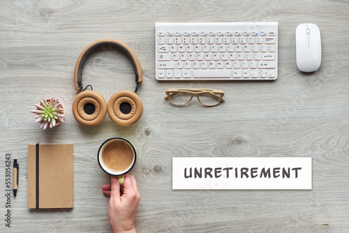 Unretirement concept image. Flat lay with modern office supplies - notebook, computer keyboard, mouse, succulent plant. Paper with text, caption Unretirement. Hand of mature worker holding coffee. photo