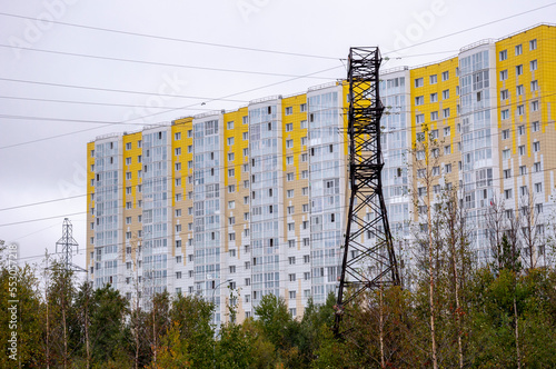 Modern urban buidings, power line, park with green trees, light blue sky