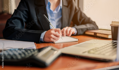 Close up Hand businesswoman in black suit and blue shirt writing or pointing on report paper on tables at coffee shop. Businesswoman,business and worker strategy concept.