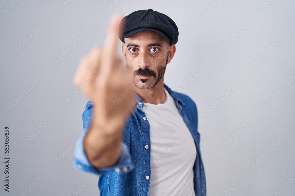 Hispanic man with beard standing over isolated background showing middle finger, impolite and rude fuck off expression Hispanic man with beard standing over isolated background showing middle finger, impolite and rude fuck off expression