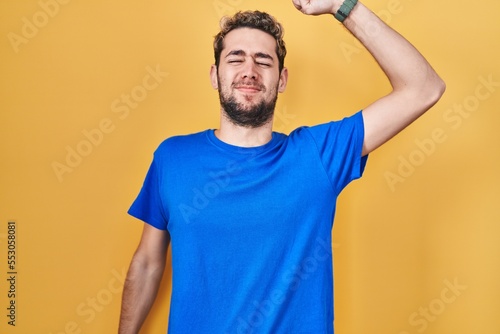 Hispanic man with beard standing over yellow background stretching back, tired and relaxed, sleepy and yawning for early morning