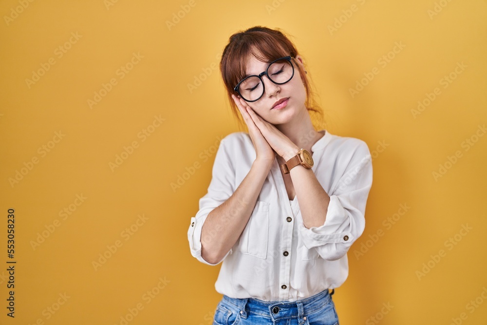 Young beautiful woman wearing casual shirt over yellow background sleeping tired dreaming and posing with hands together while smiling with closed eyes.