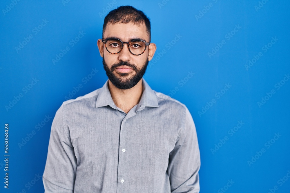 Fototapeta premium Middle east man with beard standing over blue background relaxed with serious expression on face. simple and natural looking at the camera.
