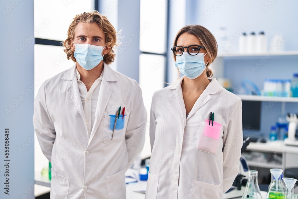 Man and woman wearing scientist uniform and medical mask at laboratory Man and woman wearing scientist uniform and medical mask at laboratory