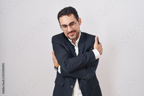 Handsome business hispanic man standing over white background hugging oneself happy and positive, smiling confident. self love and self care