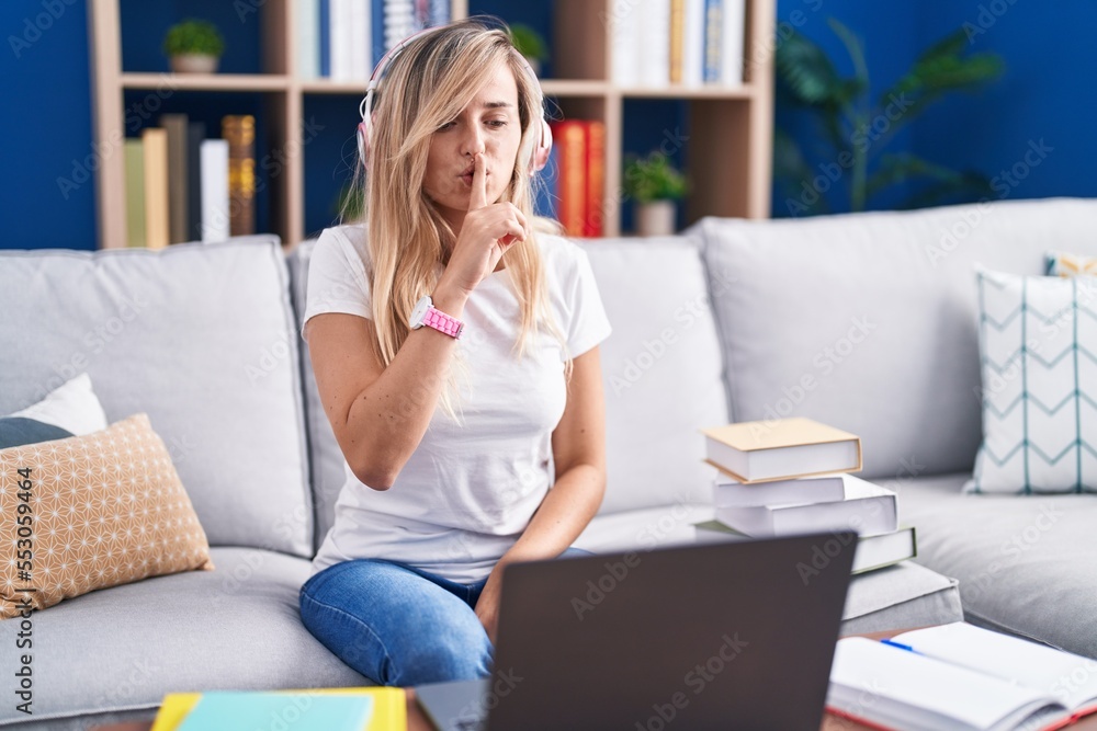 Young blonde woman studying using computer laptop at home asking to be quiet with finger on lips. silence and secret concept. Young blonde woman studying using computer laptop at home asking to be quiet with finger on lips. silence and secret concept.