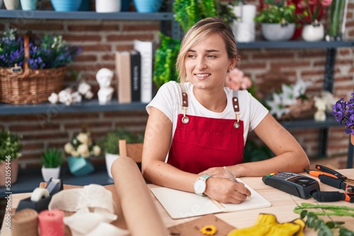 Young blonde woman florist smiling confident writing on notebook at florist