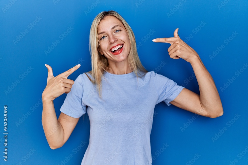 Beautiful blonde woman wearing casual t shirt over blue background smiling cheerful showing and pointing with fingers teeth and mouth. dental health concept. Beautiful blonde woman wearing casual t shirt over blue background smiling cheerful showing and pointing with fingers teeth and mouth. dental health concept.