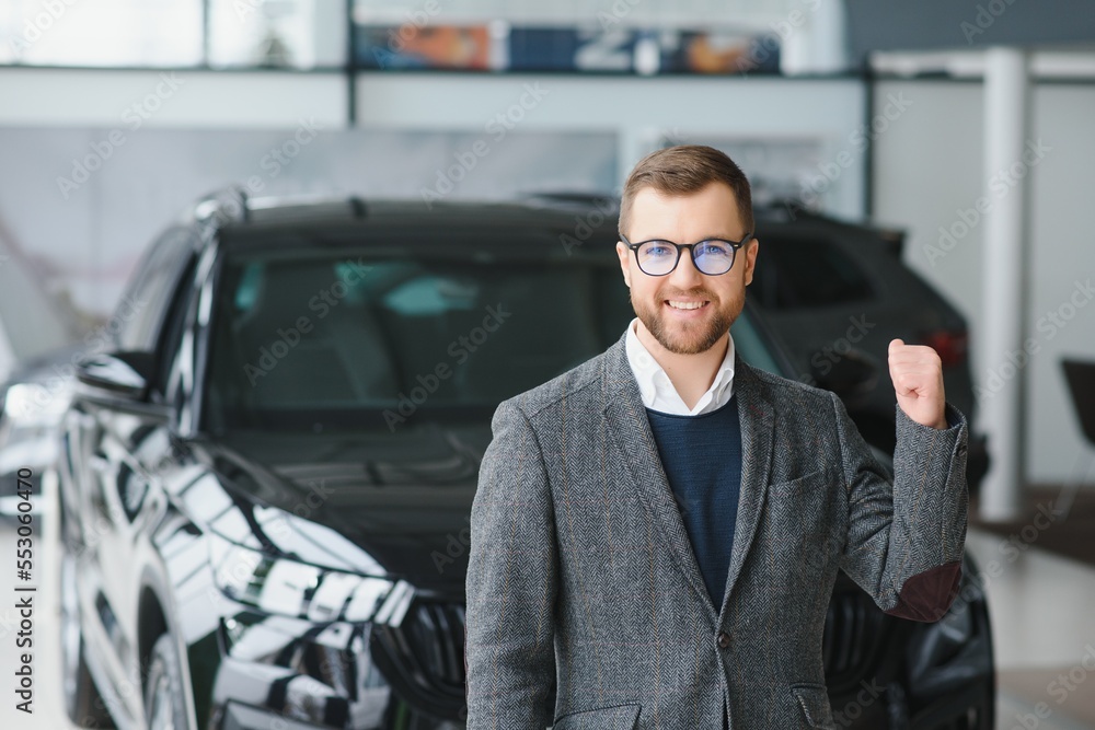 Portrait of a handsome salesman in the suit standing near the car in the showroom Portrait of a handsome salesman in the suit standing near the car in the showroom