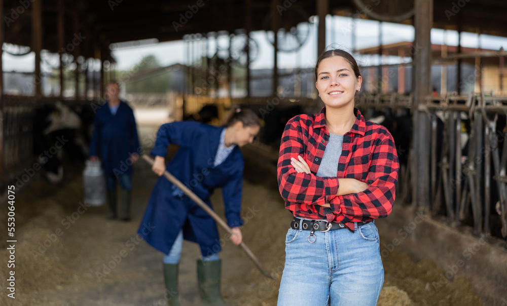 Portrait of successful young girl farmer standing in open cowshed at dairy cow farm..