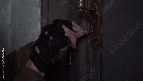 A burglar tries to open a door with an old lock with a master key, close-up hands