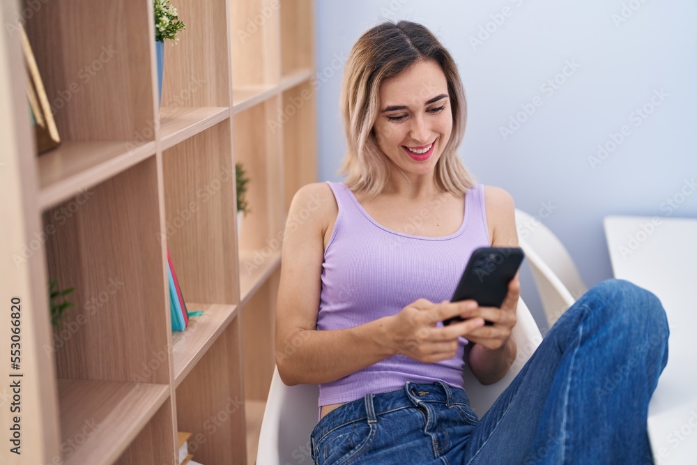 Young woman using smartphone sitting on chair at home Young woman using smartphone sitting on chair at home