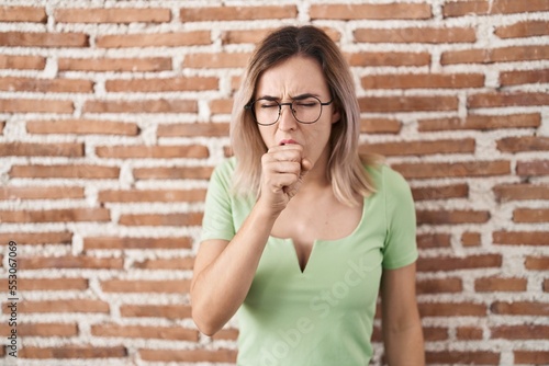 Young beautiful woman standing over bricks wall feeling unwell and coughing as symptom for cold or bronchitis. health care concept.