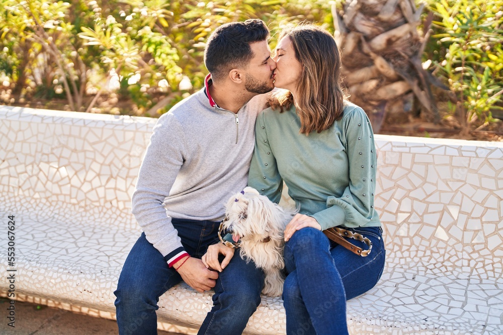 Man and woman holding dog hugging each other kissing at park Man and woman holding dog hugging each other kissing at park