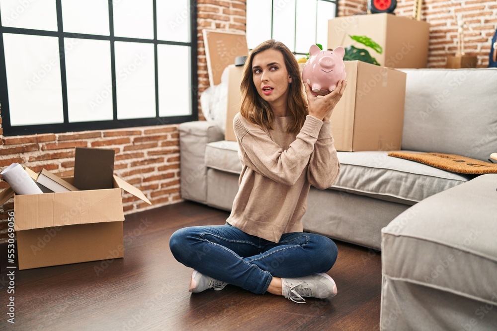 Fototapeta premium Young woman holding piggy bank at new home