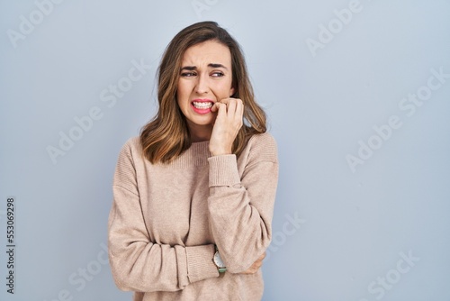 Young woman standing over isolated background looking stressed and nervous with hands on mouth biting nails. anxiety problem.
