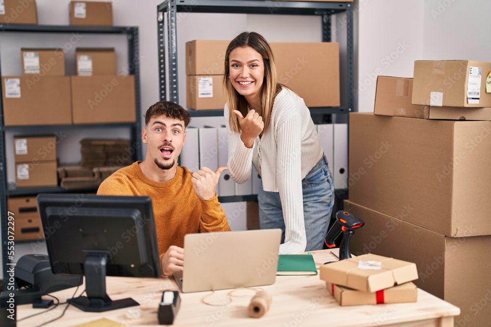 Young couple working at small business ecommerce pointing thumb up to the side smiling happy with open mouth Young couple working at small business ecommerce pointing thumb up to the side smiling happy with open mouth