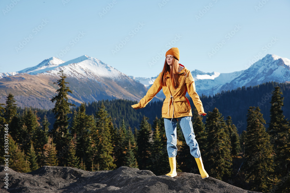 Woman full-length hiker in yellow raincoat running on a mountain trip in the fall and hiking in the mountains at sunset freedom
